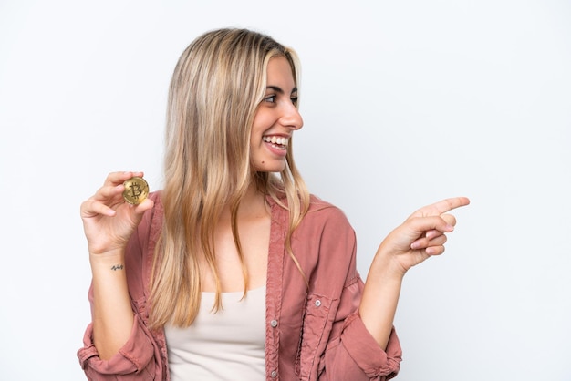 Mujer caucásica joven que sostiene un Bitcoin aislado en el fondo blanco que señala al lado para presentar un producto