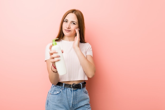 Mujer caucásica joven que sostiene una botella de crema