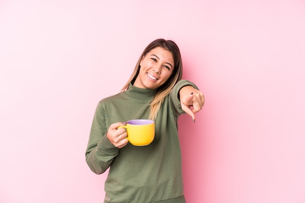 La mujer caucásica joven que sostiene un café sonríe alegre que señala al frente.