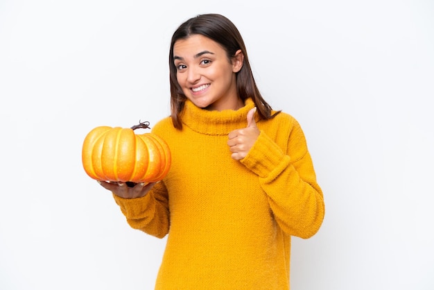 Mujer caucásica joven que sostiene una calabaza aislada en el fondo blanco que da un gesto del pulgar hacia arriba