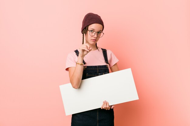 Mujer caucásica joven que sostiene un cartel que muestra el número uno con el dedo.