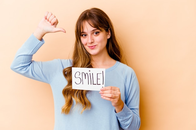 La mujer caucásica joven que sostiene un cartel de la sonrisa aislada se siente orgullosa y segura de sí misma, ejemplo a seguir.