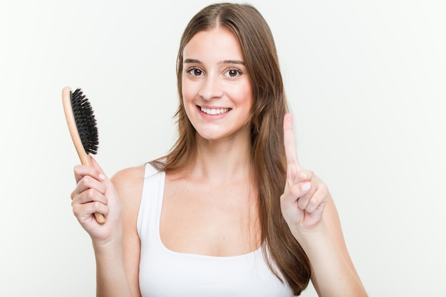 Mujer caucásica joven que sostiene un cepillo de pelo que muestra el número uno con el dedo.