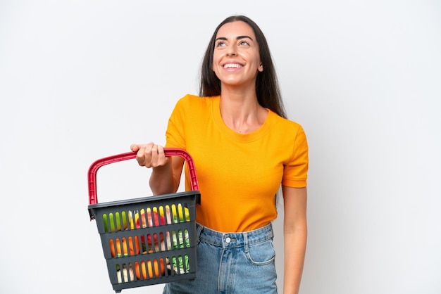 Mujer caucásica joven que sostiene una cesta de compras llena de comida