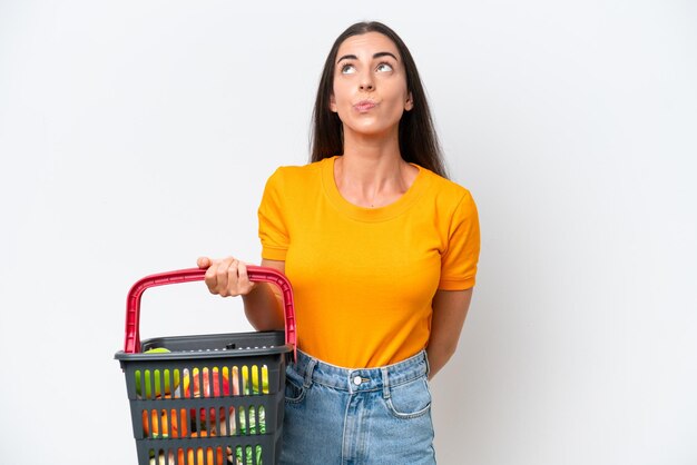 Mujer caucásica joven que sostiene una cesta de compras llena de comida