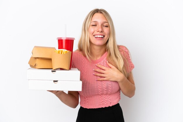 Mujer caucásica joven que sostiene la comida gorda aislada en el fondo azul que sonríe mucho