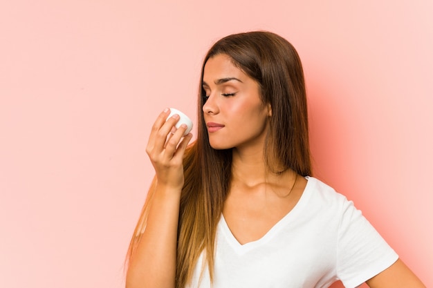 Mujer caucásica joven que sostiene una crema hidratante en una pared rosada