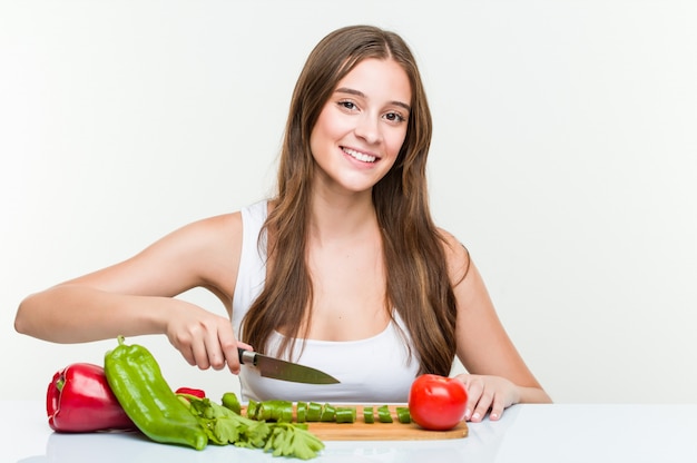 Mujer caucásica joven que sostiene un cuchillo y que corta verduras