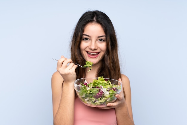 Mujer caucásica joven que sostiene una ensalada aislada en la pared azul