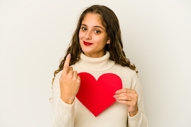 Mujer caucásica joven que sostiene una forma del día de San Valentín del corazón aislada que señala con el dedo en usted como invitando a acercarse.