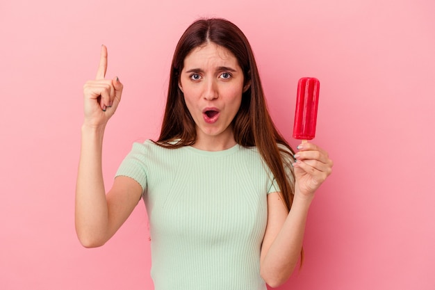 Mujer caucásica joven que sostiene un helado aislado en la pared azul que tiene una idea, concepto de la inspiración.