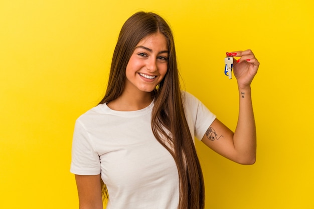 Mujer caucásica joven que sostiene una llave de la casa aislada en fondo amarillo feliz, sonriente y alegre.