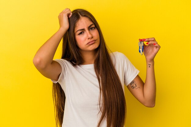 Mujer caucásica joven que sostiene las llaves de una casa aisladas en la pared amarilla que está sorprendida, ella ha recordado la reunión importante.