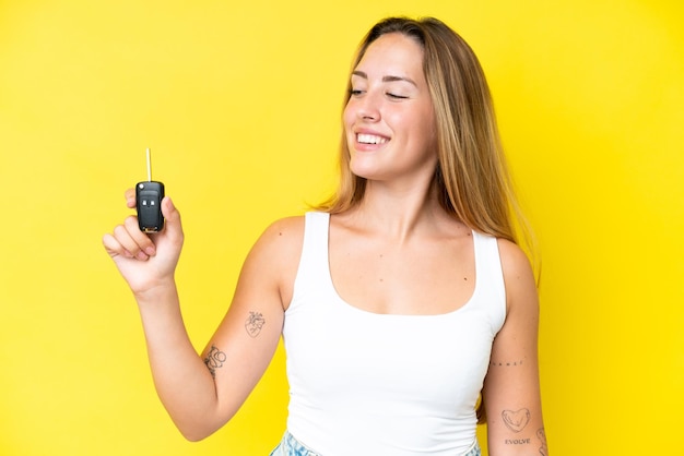 Mujer caucásica joven que sostiene las llaves del coche aislado sobre fondo amarillo con expresión feliz