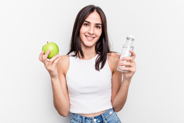 Mujer caucásica joven que sostiene la manzana y una botella de agua aislada en el fondo blanco