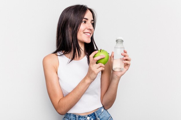 Mujer caucásica joven que sostiene la manzana y una botella de agua aislada en el fondo blanco