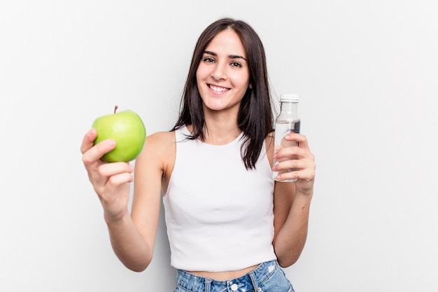 Mujer caucásica joven que sostiene la manzana y una botella de agua aislada en el fondo blanco