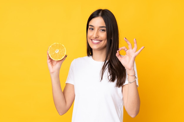 Mujer caucásica joven que sostiene una naranja aislada en amarillo