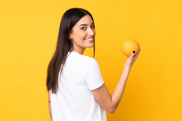 Mujer caucásica joven que sostiene una naranja sobre la pared amarilla