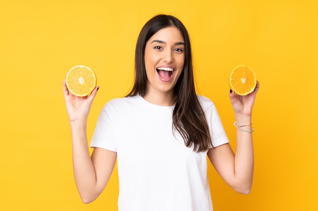 Mujer caucásica joven que sostiene una naranja sobre la pared amarilla