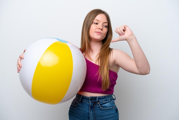 Mujer caucásica joven que sostiene la pelota de playa aislada en el fondo blanco orgullosa y satisfecha