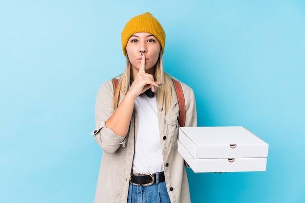 Mujer caucásica joven que sostiene las pizzas aisladas guardando un secreto o pidiendo silencio.