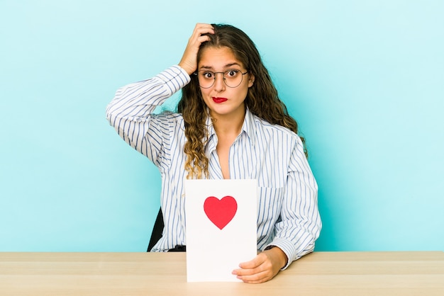 Mujer caucásica joven que sostiene una tarjeta del día de San Valentín aislada que está sorprendida, ella ha recordado la reunión importante.