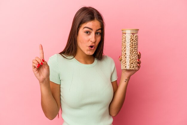 Mujer caucásica joven que sostiene un tarro de garbanzos aislado en la pared rosada que tiene una gran idea, concepto de creatividad.