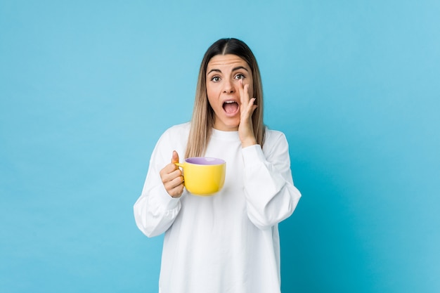 Mujer caucásica joven que sostiene una taza de café que grita excitada al frente.