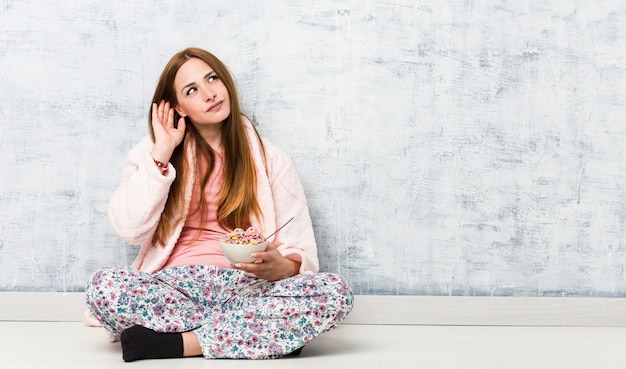 Mujer caucásica joven que sostiene un tazón de cereal que intenta escuchar un chisme.