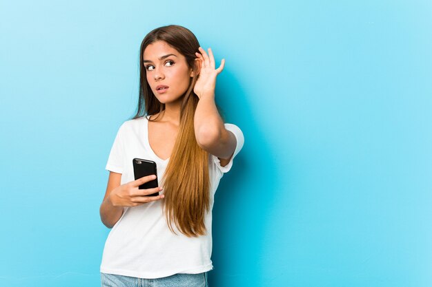 Mujer caucásica joven que sostiene un teléfono que intenta escuchar un chisme.
