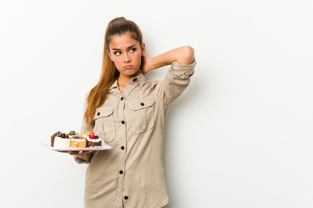 Mujer caucásica joven que sostiene las tortas dulces que tocan la parte posterior de la cabeza, pensando y tomando una decisión.