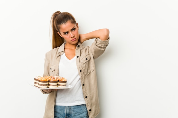 Mujer caucásica joven que sostiene las tortas dulces que tocan la parte posterior de la cabeza, pensando y tomando una decisión.