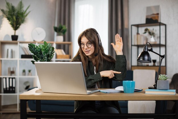 Mujer caucásica joven que usa auriculares y una computadora portátil para una conversación de video en la oficina