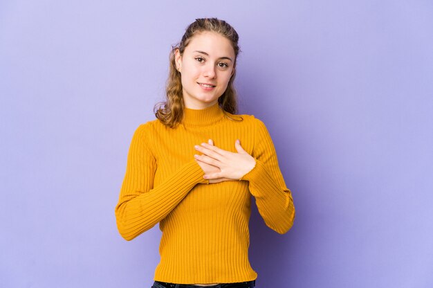 Mujer caucásica joven en la risa púrpura manteniendo las manos en el corazón, concepto de felicidad.