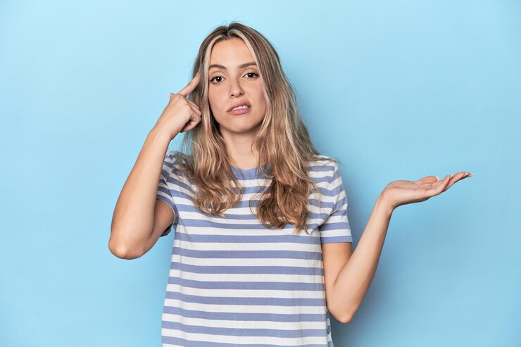 Foto mujer caucásica joven rubia en estudio azul sosteniendo y mostrando un producto en la mano