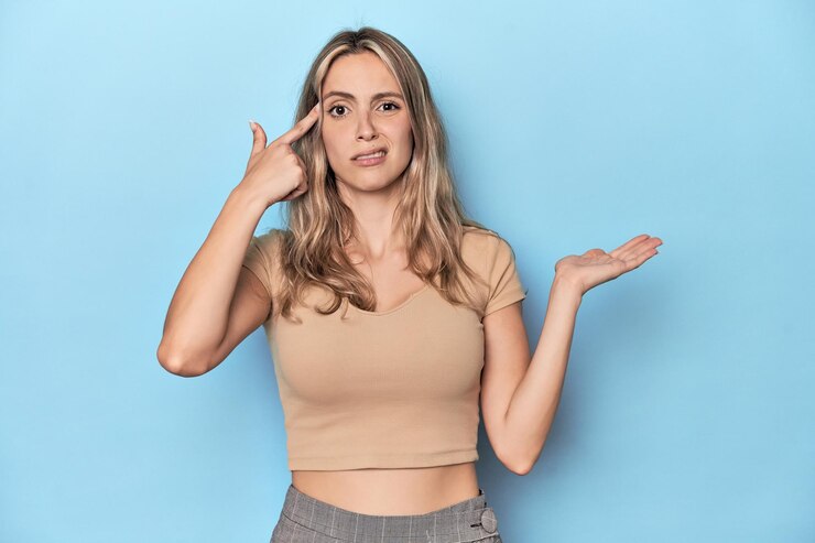 Foto mujer caucásica joven rubia en estudio azul sosteniendo y mostrando un producto en la mano