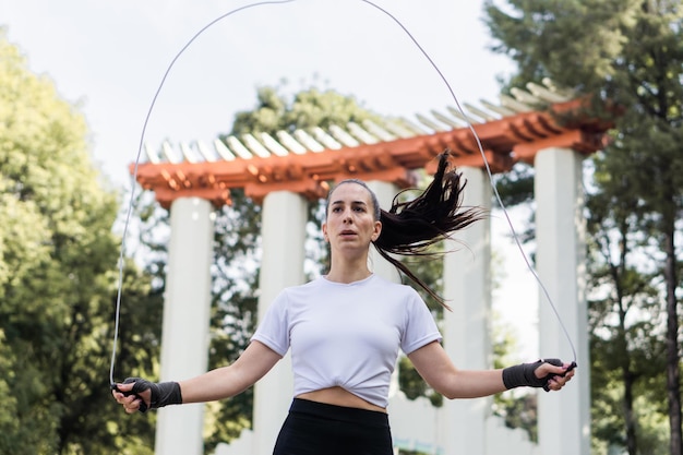 Mujer caucásica joven saltando la cuerda en un parque en ropa deportiva.