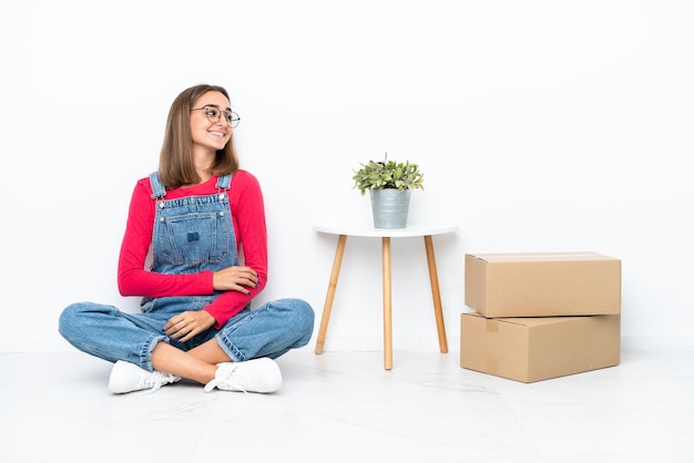 Mujer caucásica joven sentada en el suelo entre cajas feliz y sonriente