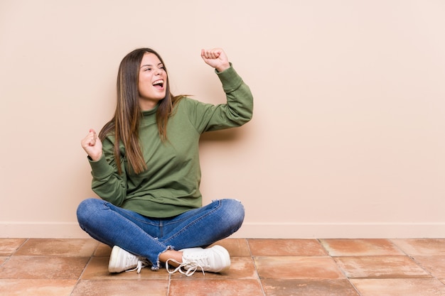 Mujer caucásica joven sentada en el suelo levantando el puño después de una victoria