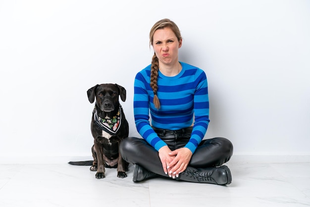 Foto mujer caucásica joven sentada en el suelo con su cachorro aislado sobre fondo blanco con expresión triste