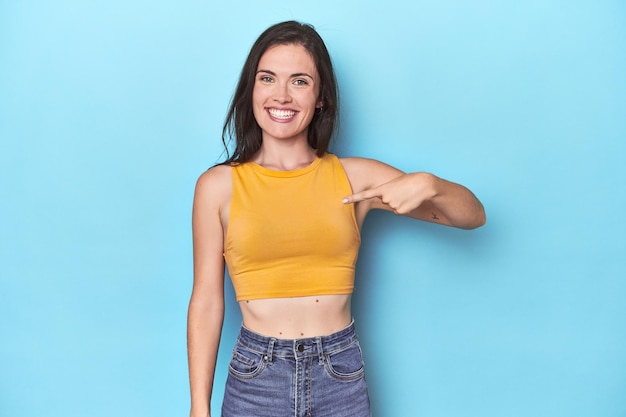 Foto mujer caucásica joven sobre fondo azul persona apuntando con la mano a un espacio de copia de camisa