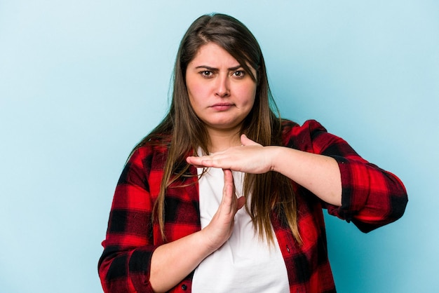 Mujer caucásica joven con sobrepeso aislada de fondo azul que muestra un gesto de tiempo de espera