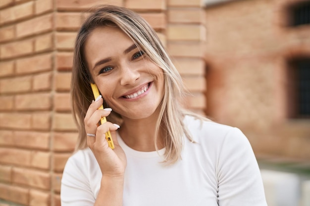 Mujer caucásica joven sonriendo confiada hablando en el teléfono inteligente en la calle