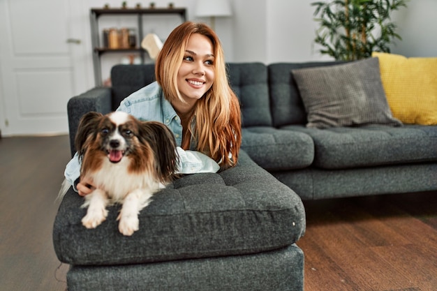 Mujer caucásica joven sonriendo confiada tumbada en el sofá con perro en casa