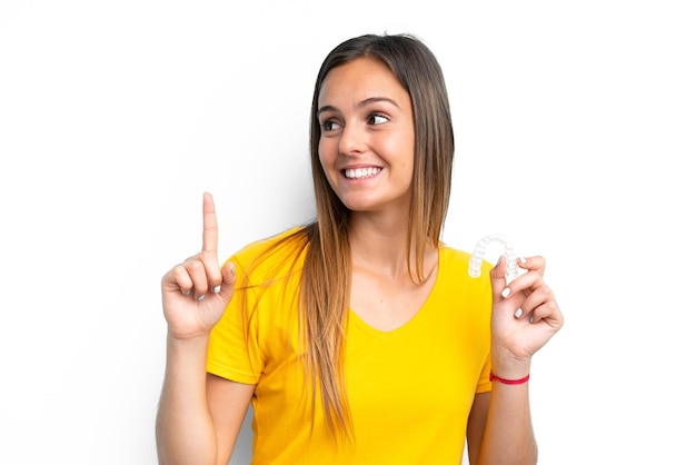 Foto mujer caucásica joven sosteniendo aparatos invisibles aislados en fondo blanco con la intención de darse cuenta de la solución mientras levanta un dedo