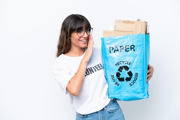 Mujer caucásica joven sosteniendo una bolsa de reciclaje llena de papel para reciclar aislado sobre fondo blanco susurrando algo