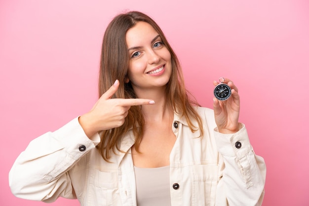 Mujer caucásica joven sosteniendo brújula aislada sobre fondo rosa y apuntándola