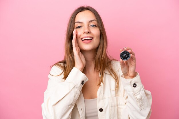 Mujer caucásica joven sosteniendo brújula aislada sobre fondo rosa gritando con la boca abierta