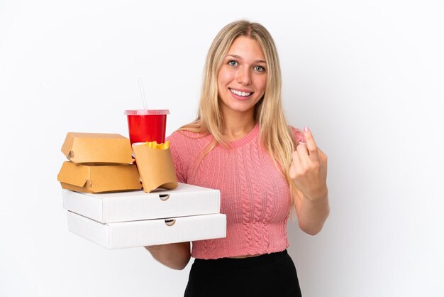 Mujer caucásica joven sosteniendo comida gorda aislada en el fondo azul haciendo el gesto de venir